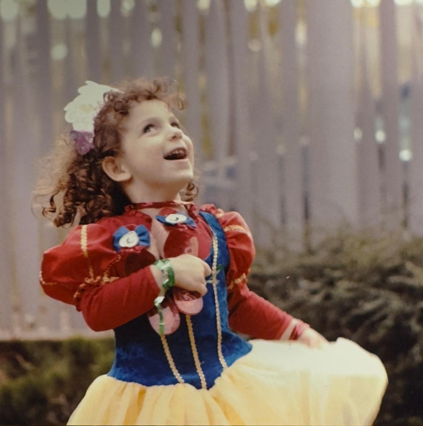 A young Esra in a Snow White costume, looking up joyfully. Drag me — the text flows around me.